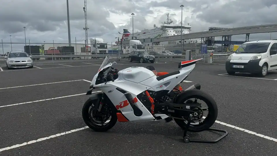 A white and orange KTM 990 RC R on a paddock stand in the port car park in Belfast, with a Stena Line ferry behind.